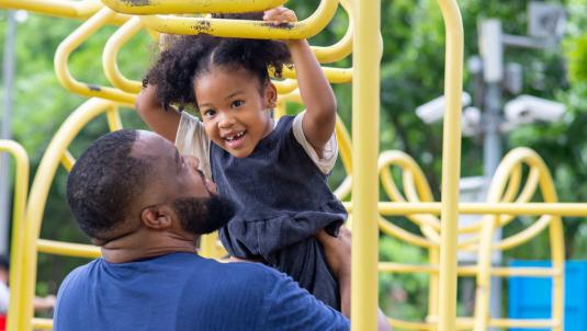 Young girl on climbing frame being held by her father