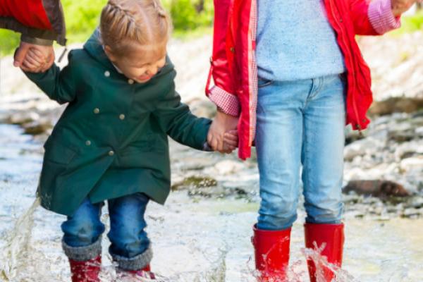 [A family holding hands and wearing wellington boots in a stream]