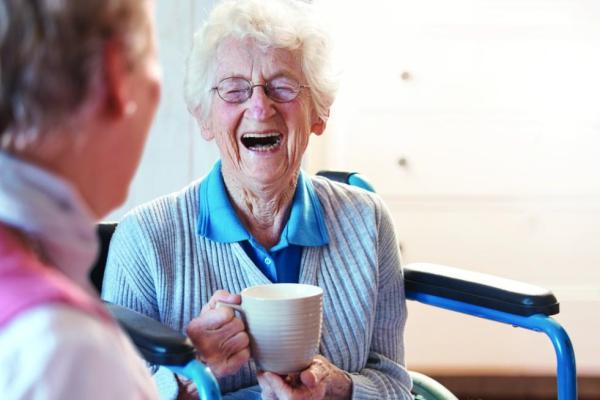 old woman laughing whilst drinking a hot drink