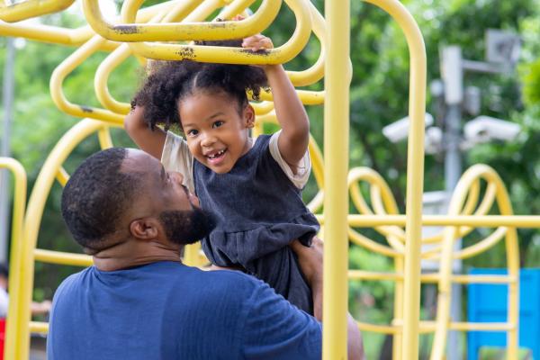 Young girl on climbing frame being held by her father