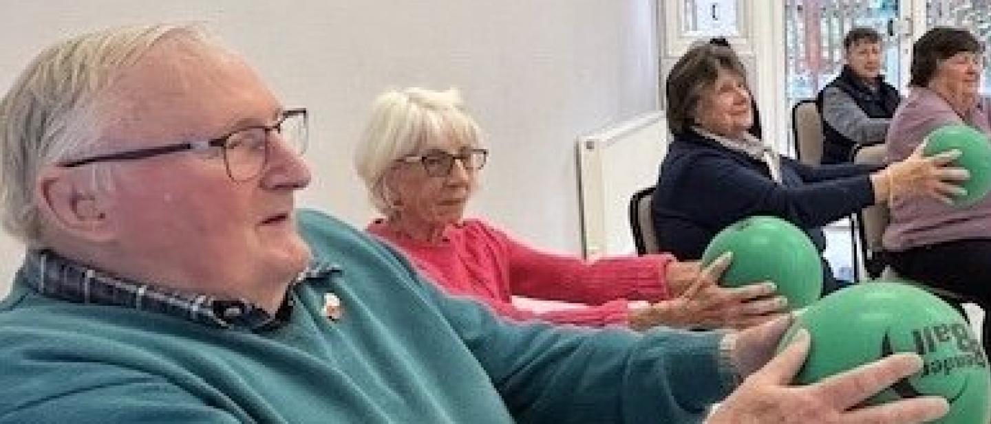 group of older people holding a balance call in front of them doing strength exercises on a chair