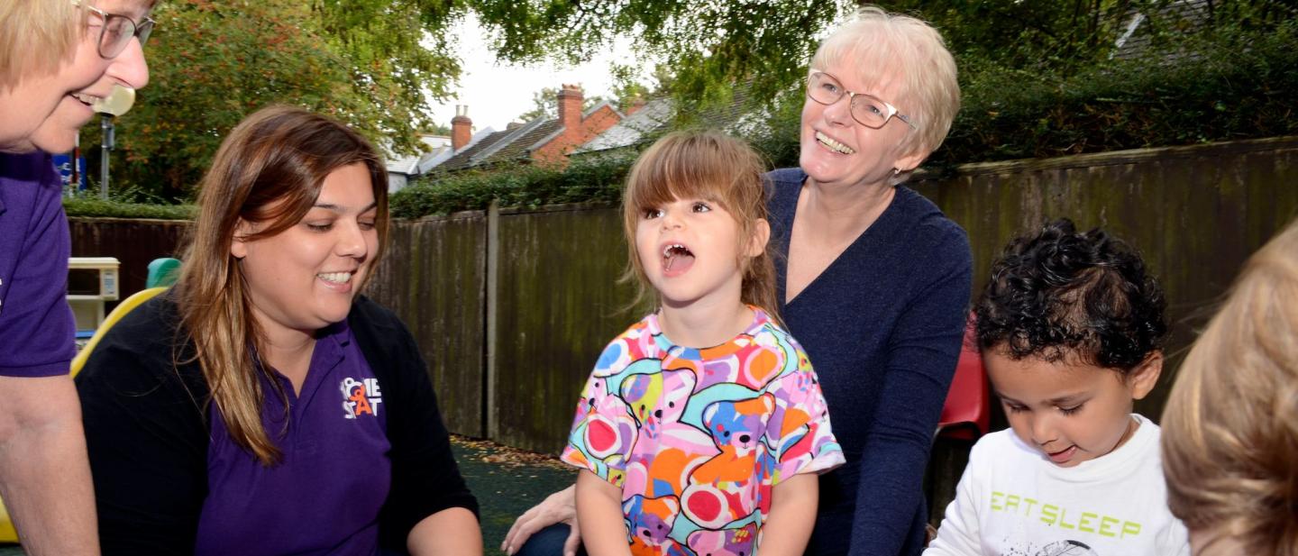 3 toddlers with staff from Home Start Surrey Heath playing outdoors with toy trucks