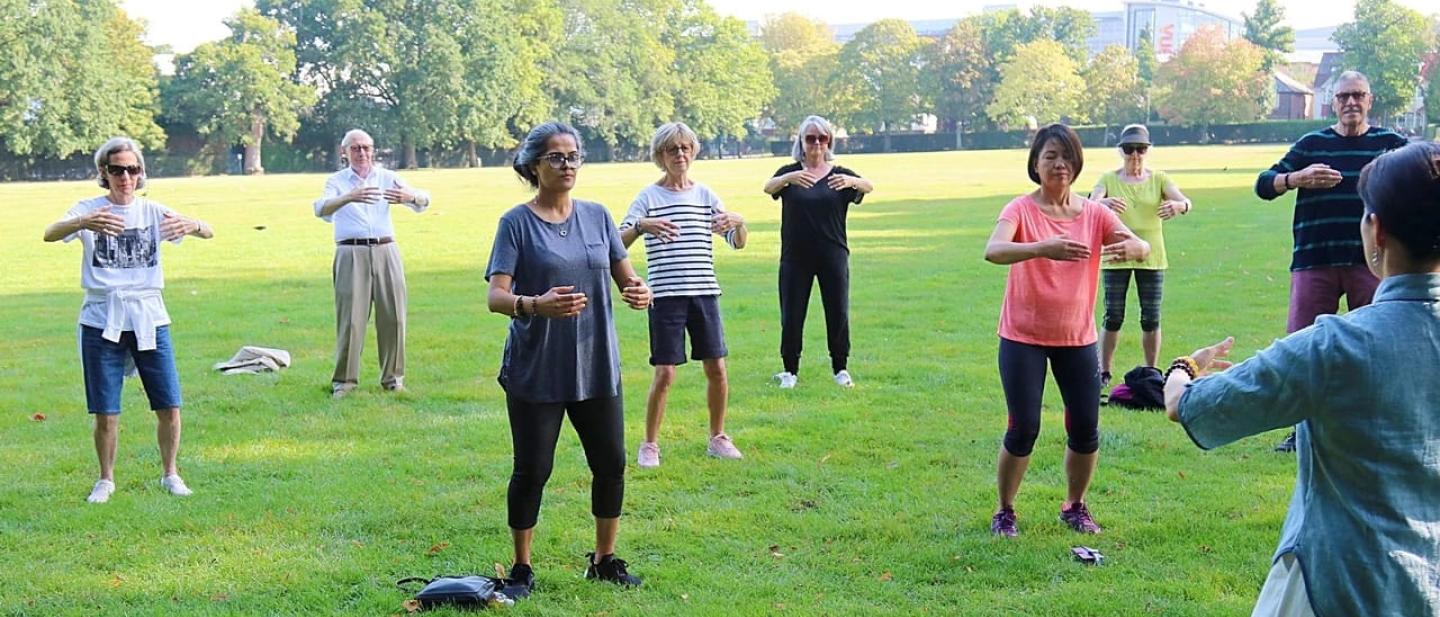 group of people practicing TaiChi and Qigong in the park led by an instructor