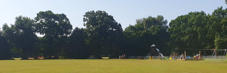 Large field at Frimley Lodge Park with view of playground