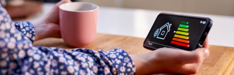 Person sat with a mug looking at energy efficiency of their home on a mobile phone