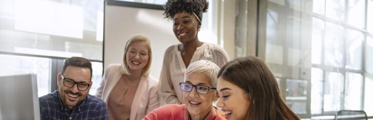 A diverse group of people gathered around a computer in the work place