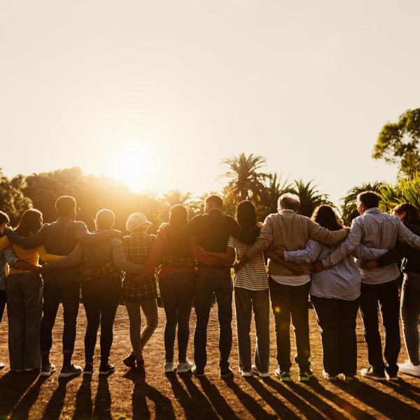 Stock image of a group of people shoulder-to-shoulder, backs facing the camera and looking up towards the sun.