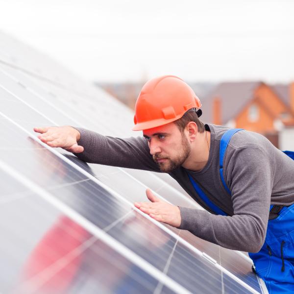 Photograph of a man wearing a hard hat installing solar panels.