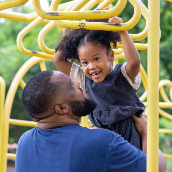Young girl on climbing frame being held by her father