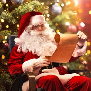 Santa reading a list in front of a Christmas tree
