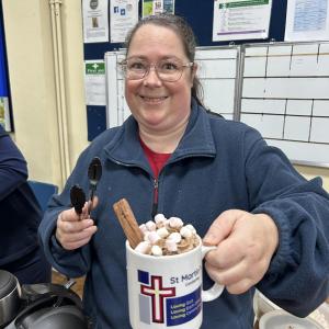church volunteer holding a large hot chocolate with cream, marshmallows and a flake on top