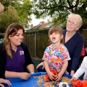 3 toddlers with staff from Home Start Surrey Heath playing outdoors with toy trucks