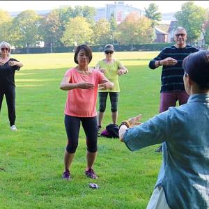 group of people practicing TaiChi and Qigong in the park led by an instructor